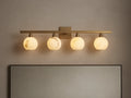 Arica Wall Sconce with four illuminated round glass shades mounted on a horizontal brass fixture above a mirror.