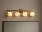 Arica Wall Sconce with four illuminated round glass shades mounted on a horizontal brass fixture above a mirror.