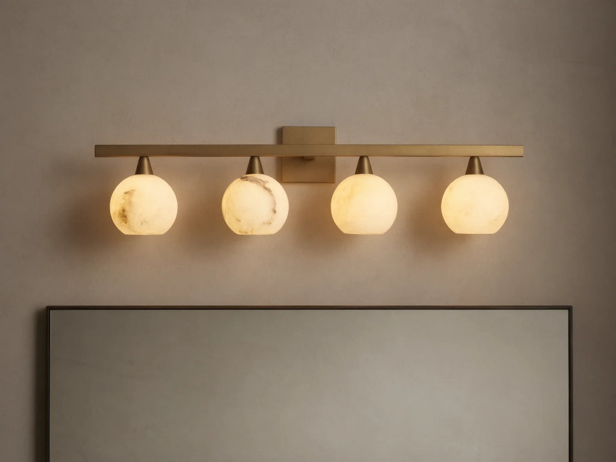 Arica Wall Sconce with four illuminated round glass shades mounted on a horizontal brass fixture above a mirror.